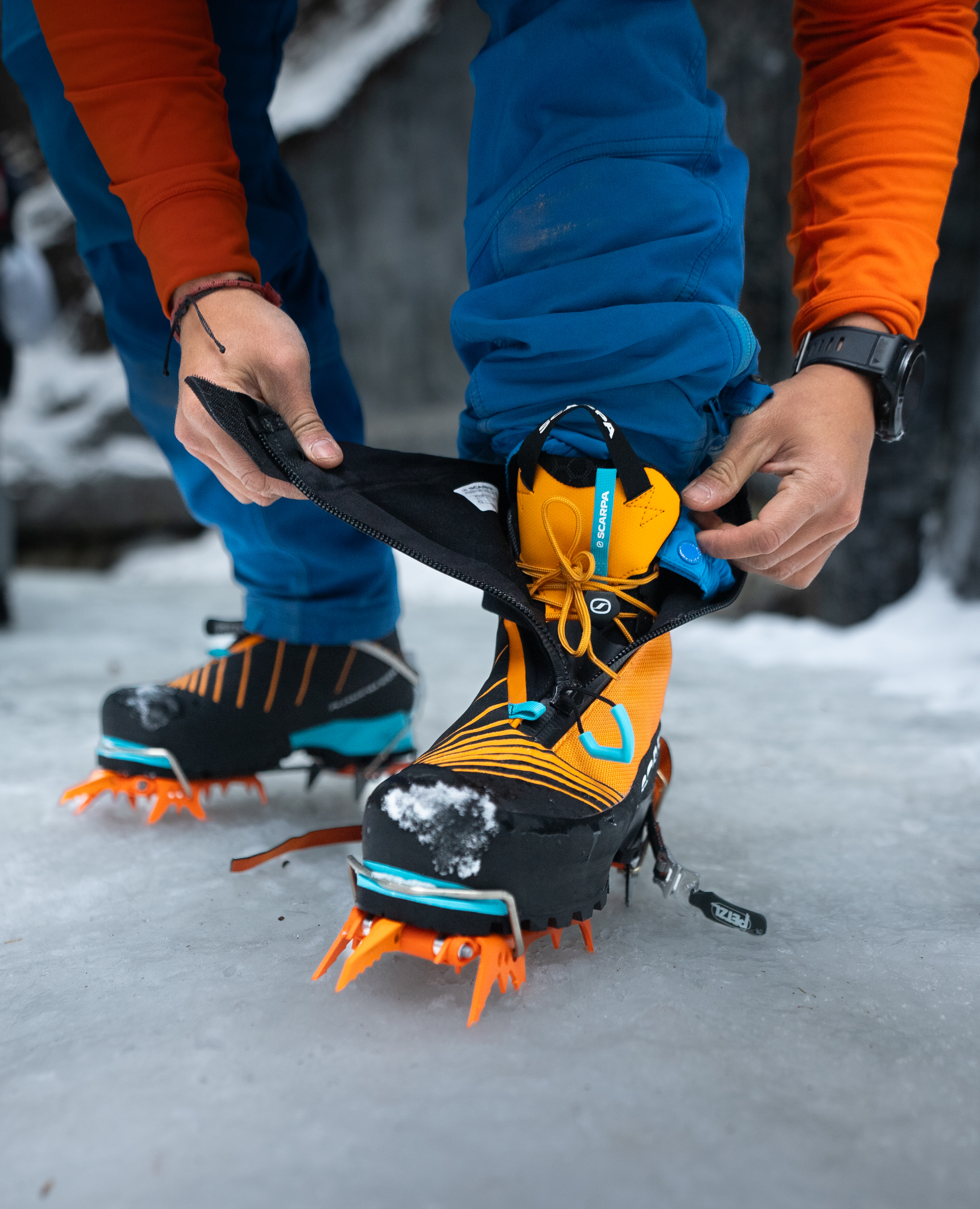 Mountaineer fitting crampons over Scarpa boots on snow wearing PrimaLoft-insulated jacket and trousers