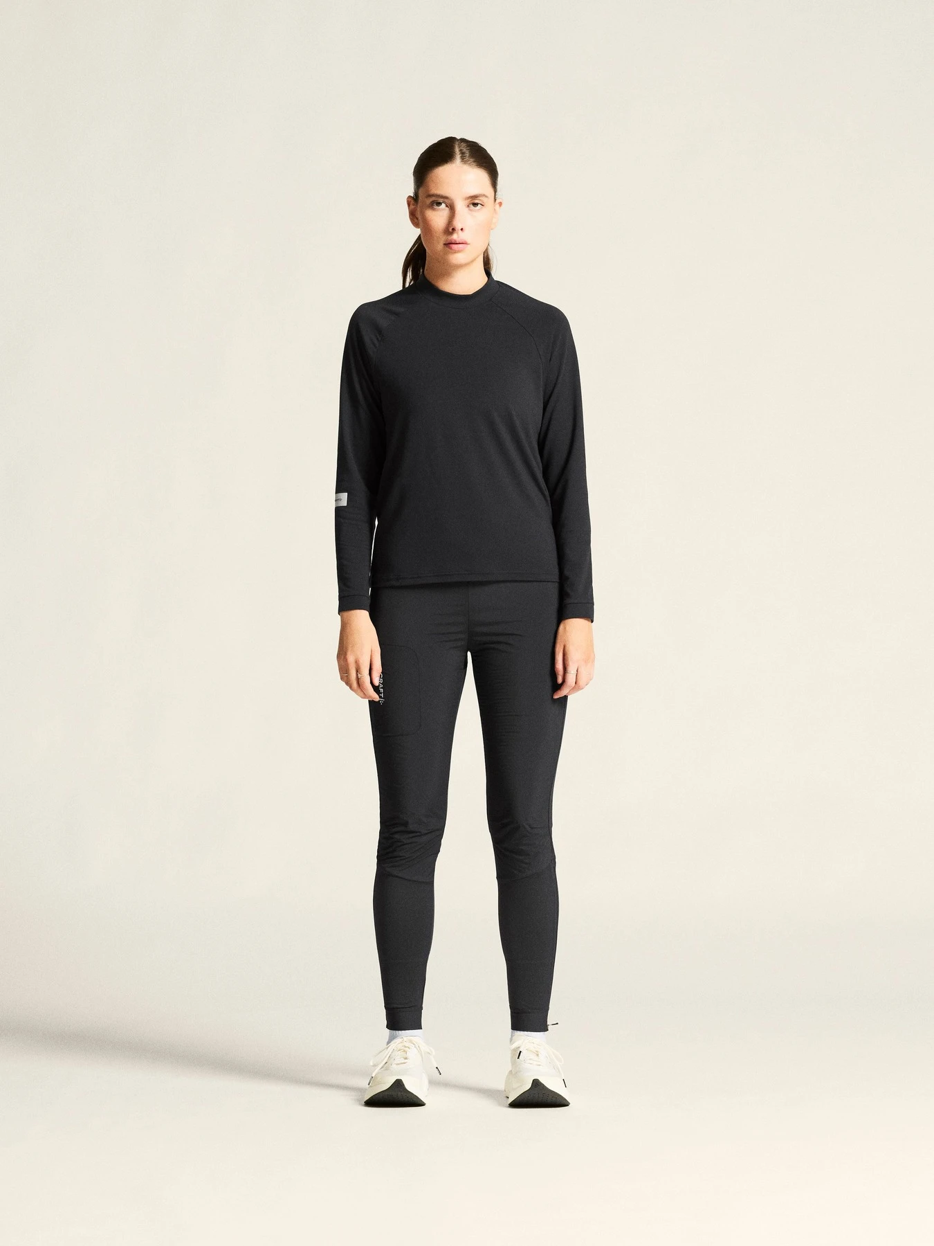 Woman wearing a black long-sleeve top, black leggings, and white sneakers, full-length front view.