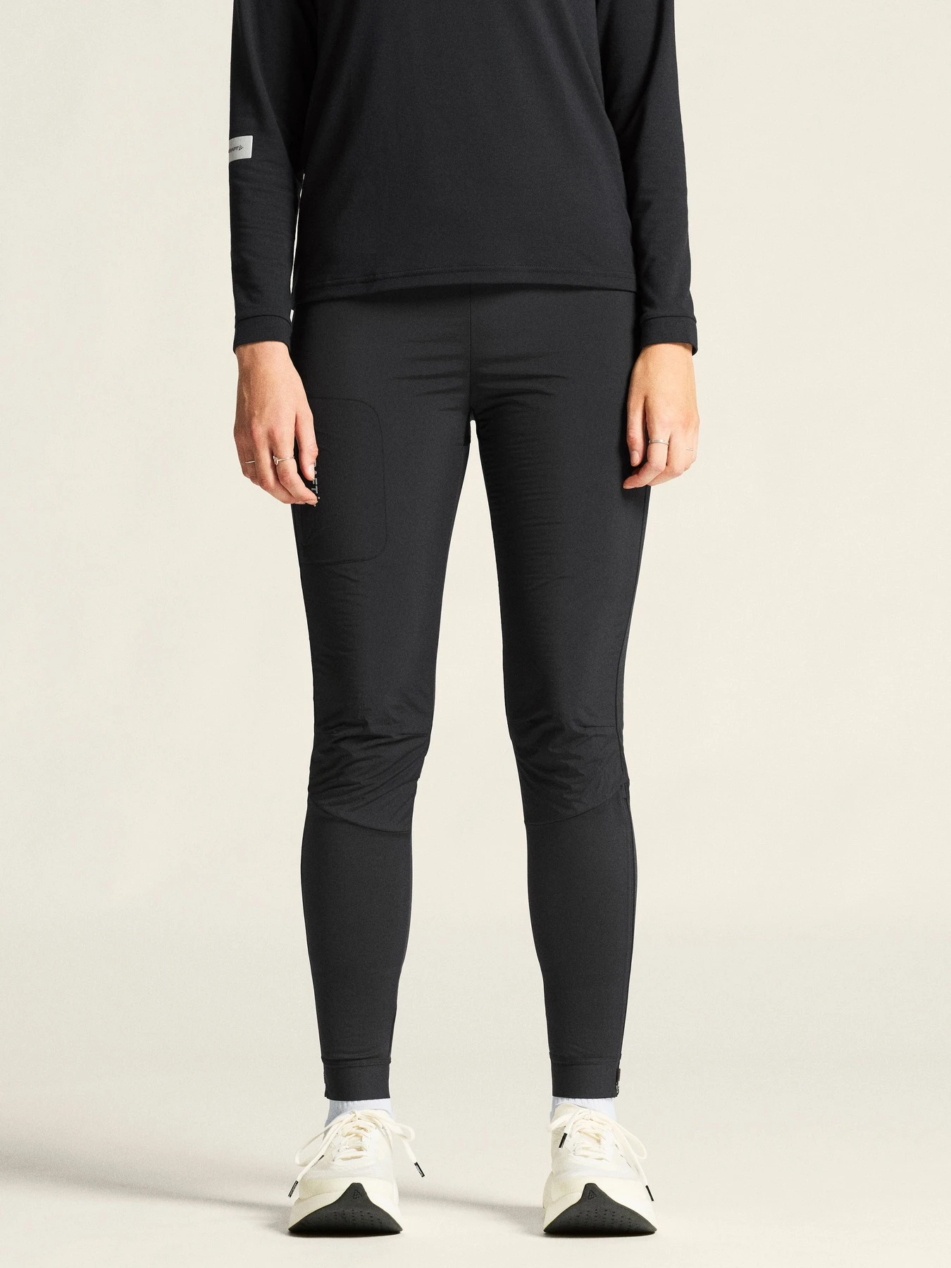 Person wearing a black long-sleeve top, black leggings, and white sneakers, front view.