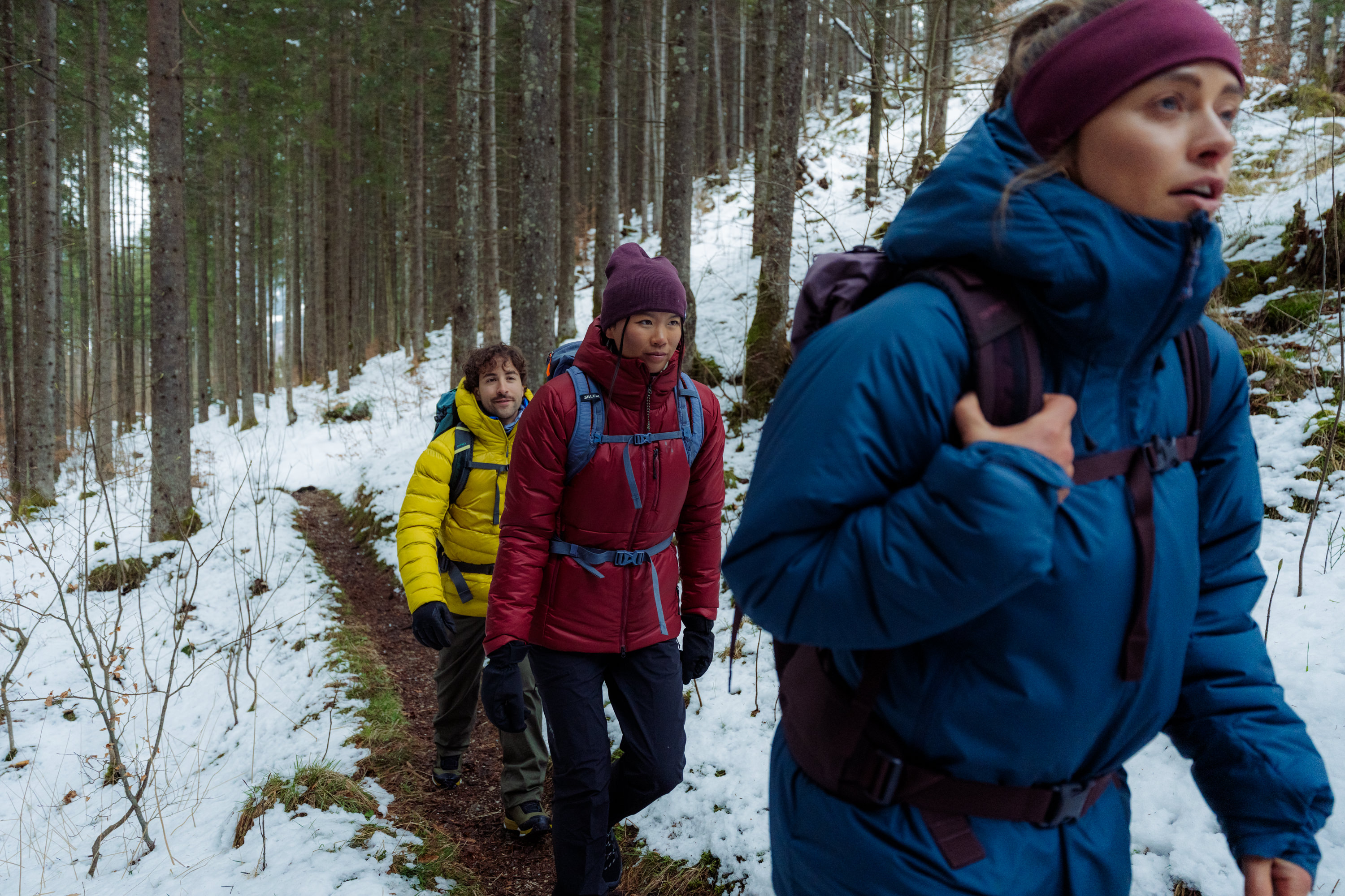 `Three hikers walking snowy forest trail wearing PrimaLoft-Rise insulated jackets