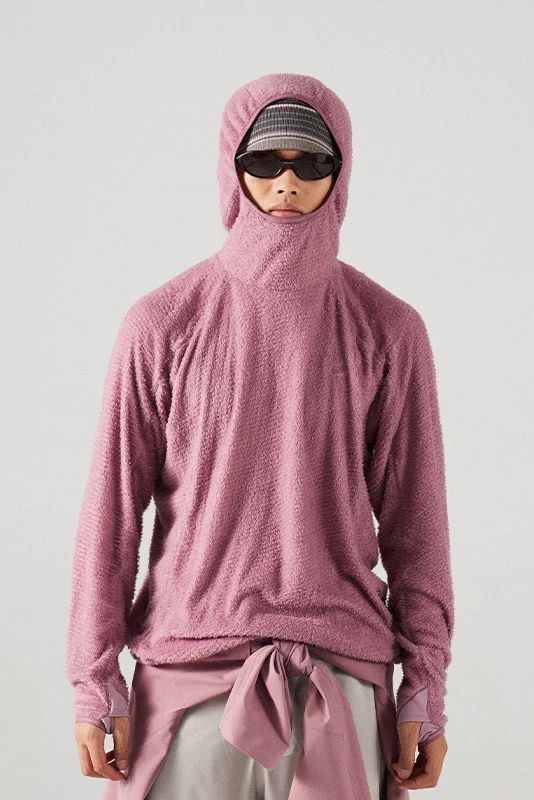 Person wearing a pink fuzzy fleece hooded pullover with the hood pulled up over the lower face, sunglasses, and a striped cap