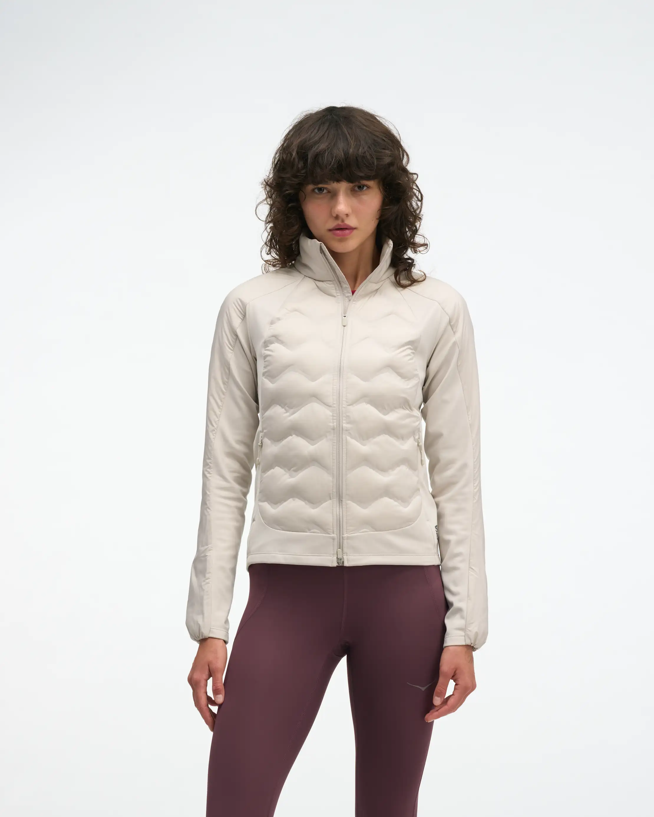Woman wearing a cream quilted hybrid jacket and burgundy leggings, front view.