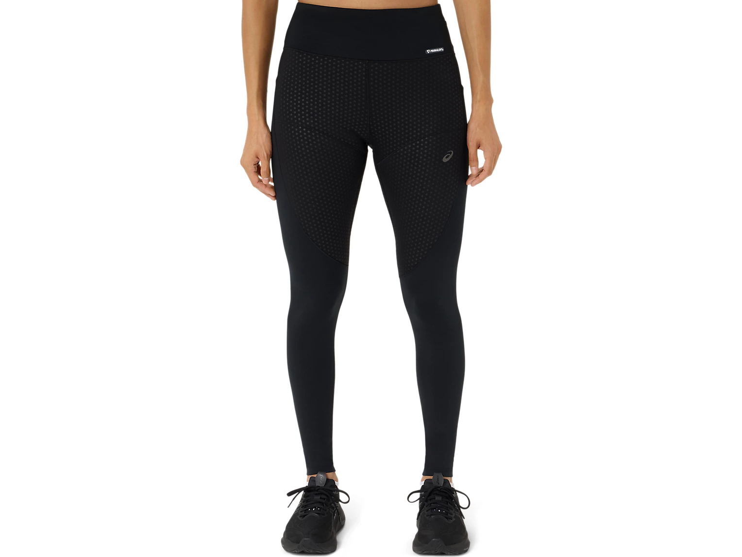 Person wearing black Asics leggings with a textured front panel and a PrimaLoft waistband label, with black sneakers.