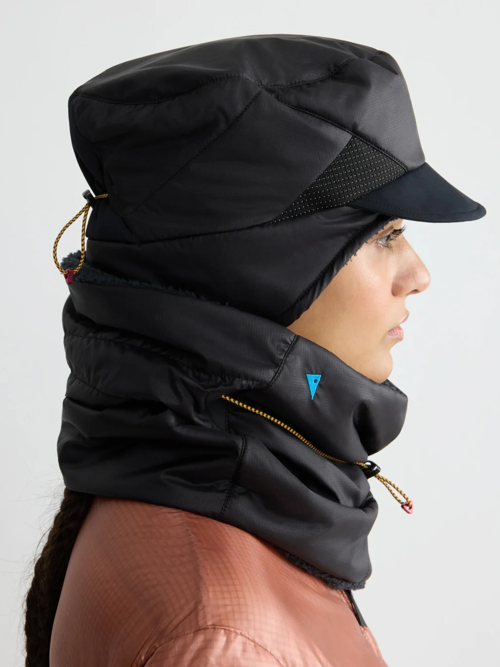 Person in side profile wearing a black insulated cap with a visor and a matching neck gaiter.