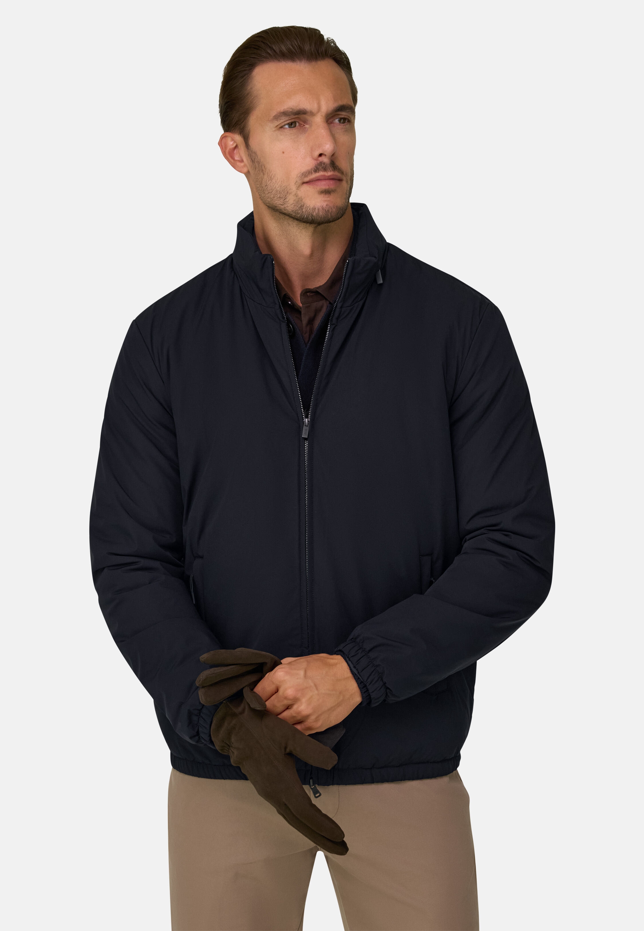 Man wearing a navy zip-up jacket and khaki pants, putting on a pair of gloves, front view.