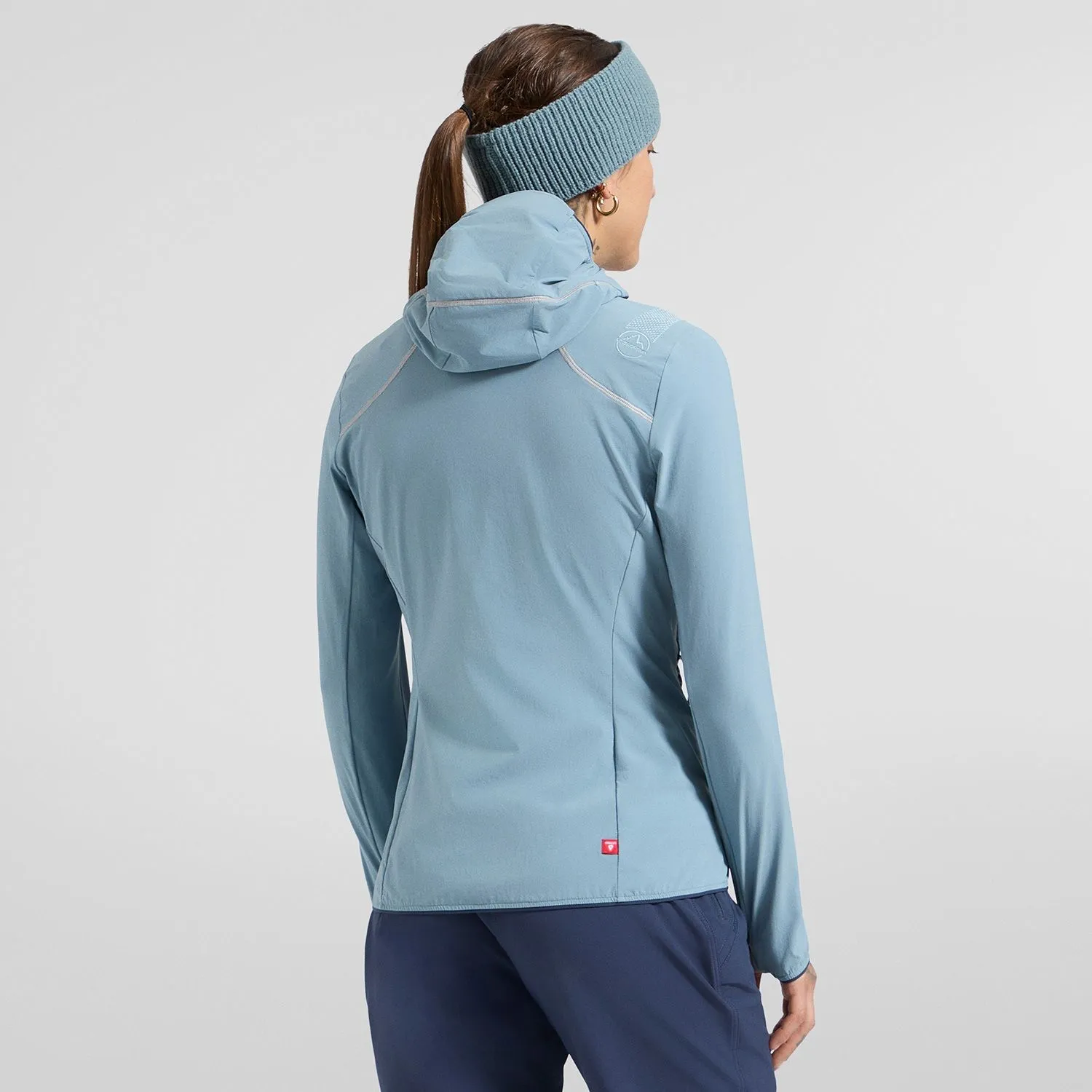 Woman wearing a light blue La Sportiva hooded jacket and matching headband, back view.