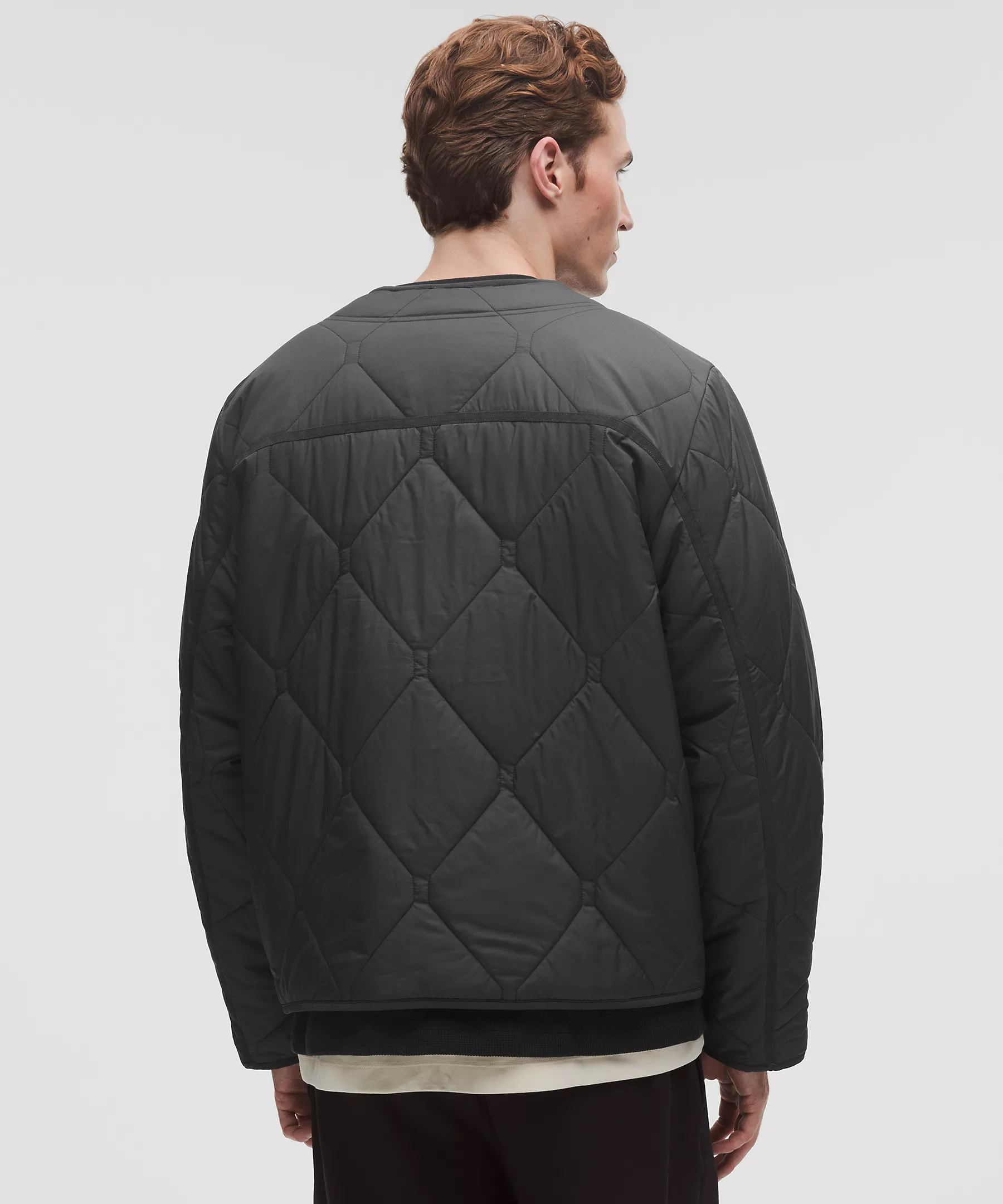 Man wearing a black diamond-quilted collarless jacket, back view.