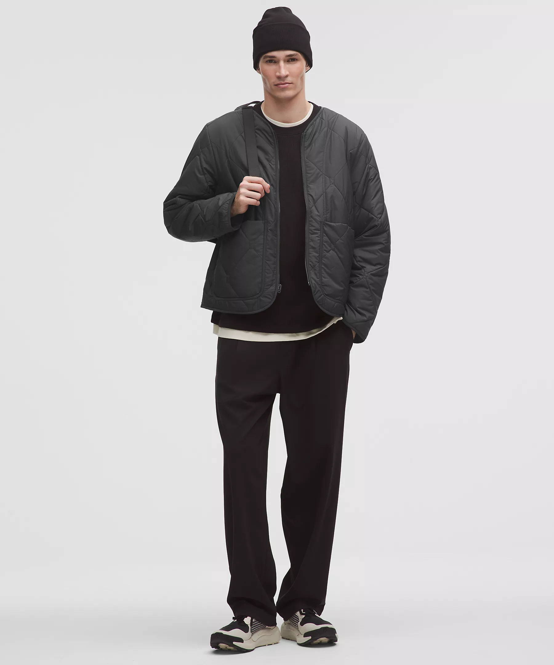 Man wearing a black collarless diamond-quilted jacket and beanie, front view.
