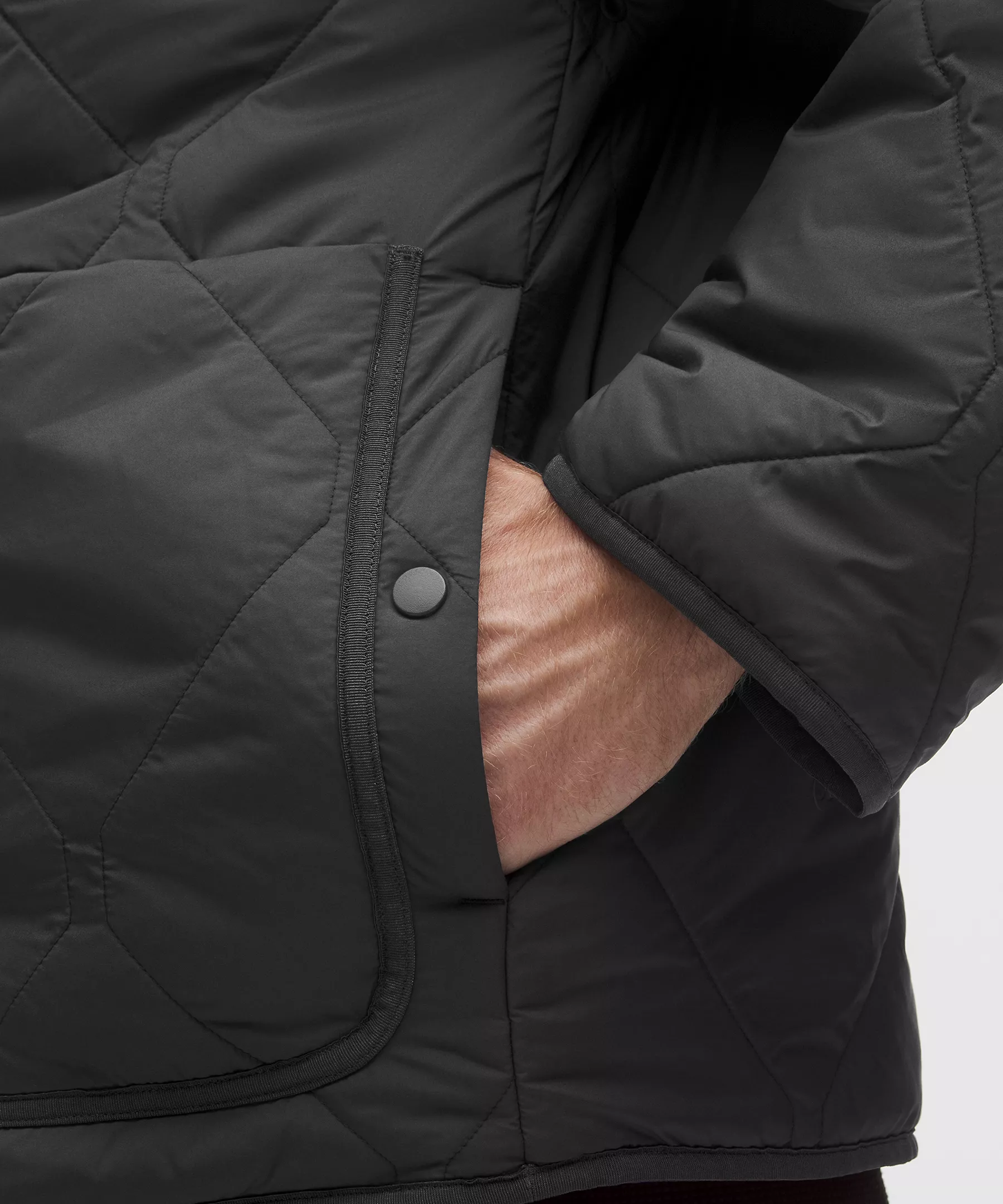 Close-up of a hand in the pocket of a black diamond-quilted jacket, snap button visible.