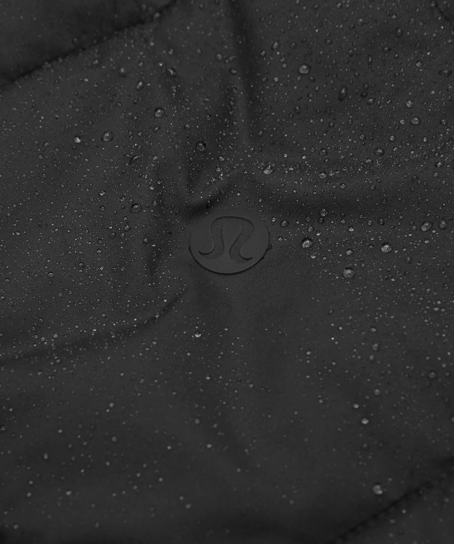 Close-up of black diamond-quilted fabric with a Lululemon logo, water droplets visible