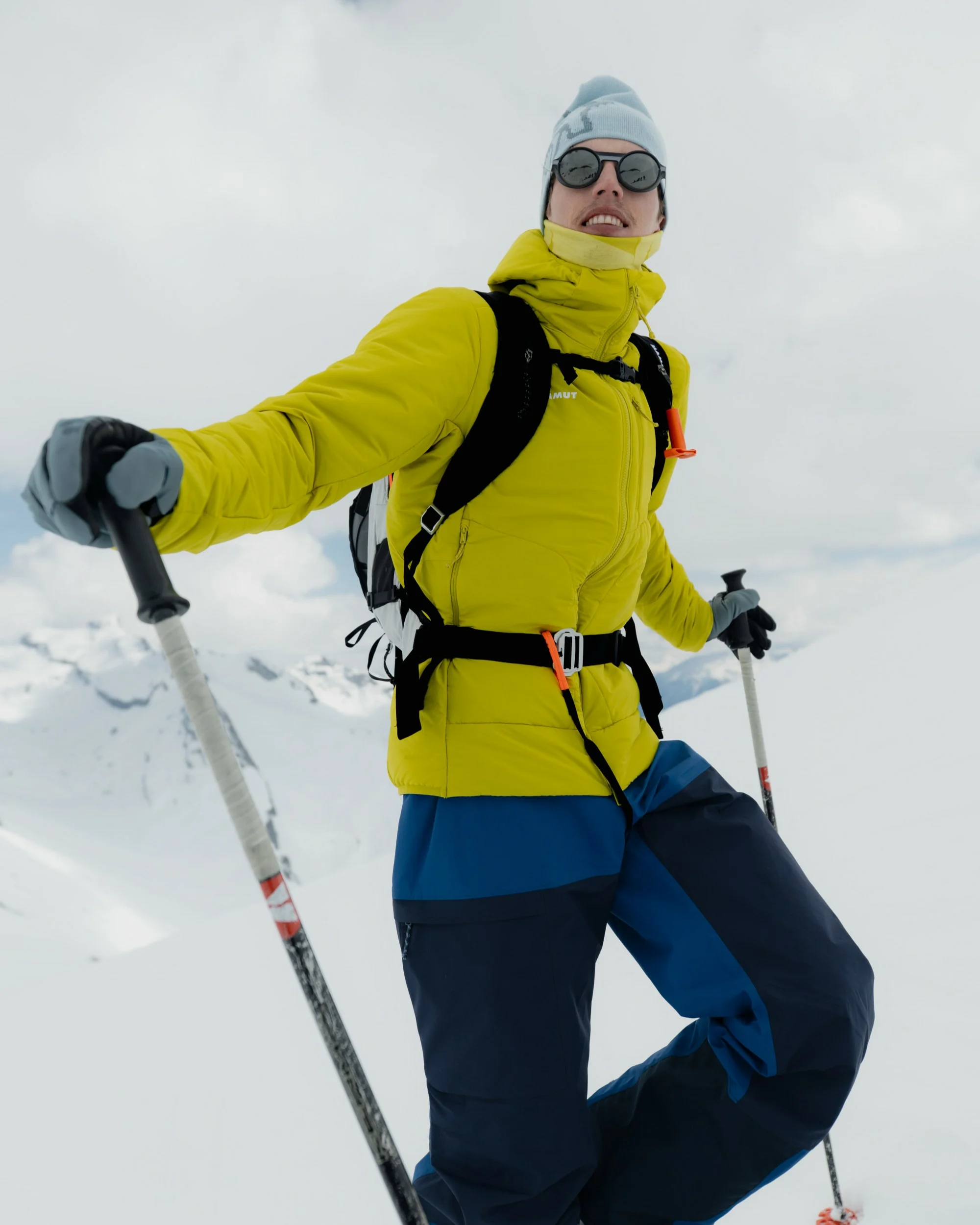 Man in a yellow-green jacket, goggles, and backpack holding ski poles on a snowy slope.