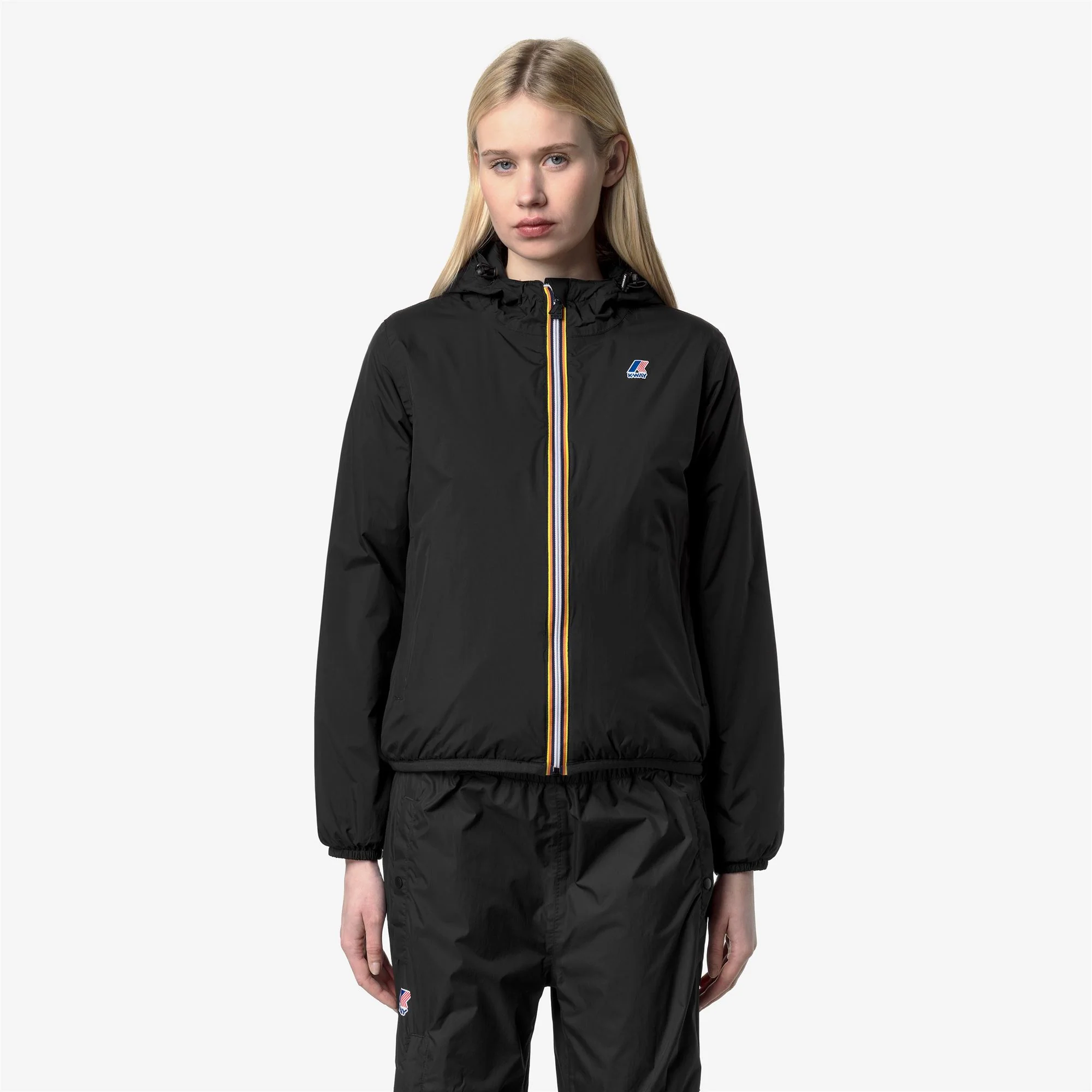 Woman wearing a black K-Way hooded jacket and matching pants, front view