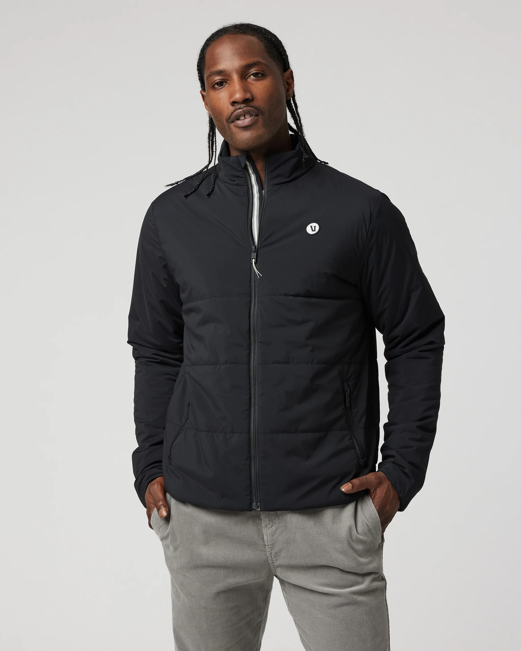Man wearing a black quilted jacket over gray pants, front view.