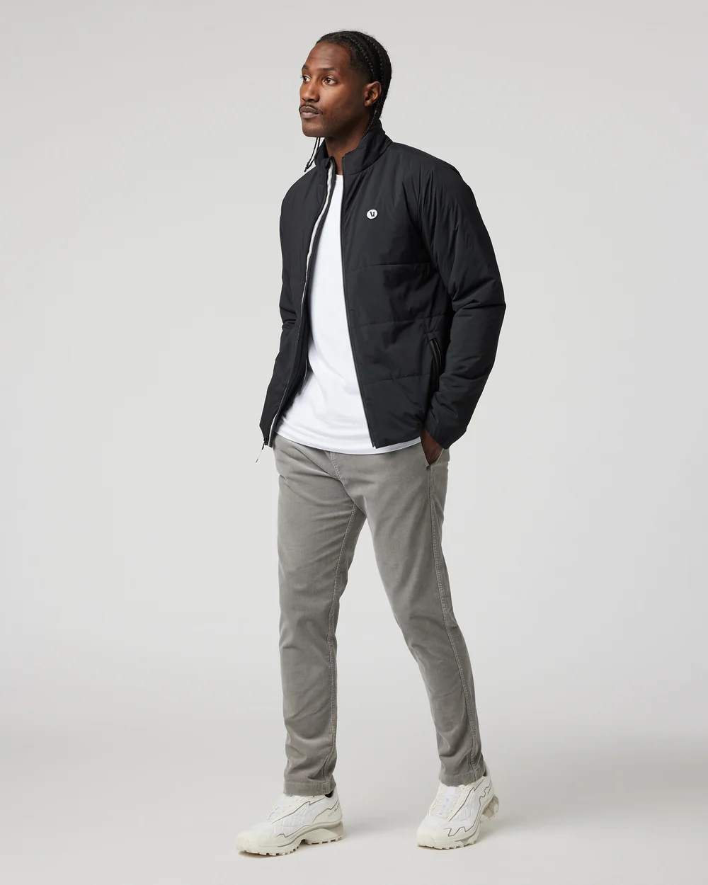 Man wearing a black quilted Vuori jacket over a white shirt, full-length front view