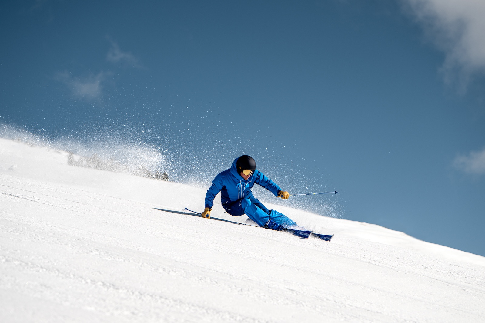 Skier wearing a blue jacket carving down a snowy slope, action shot.