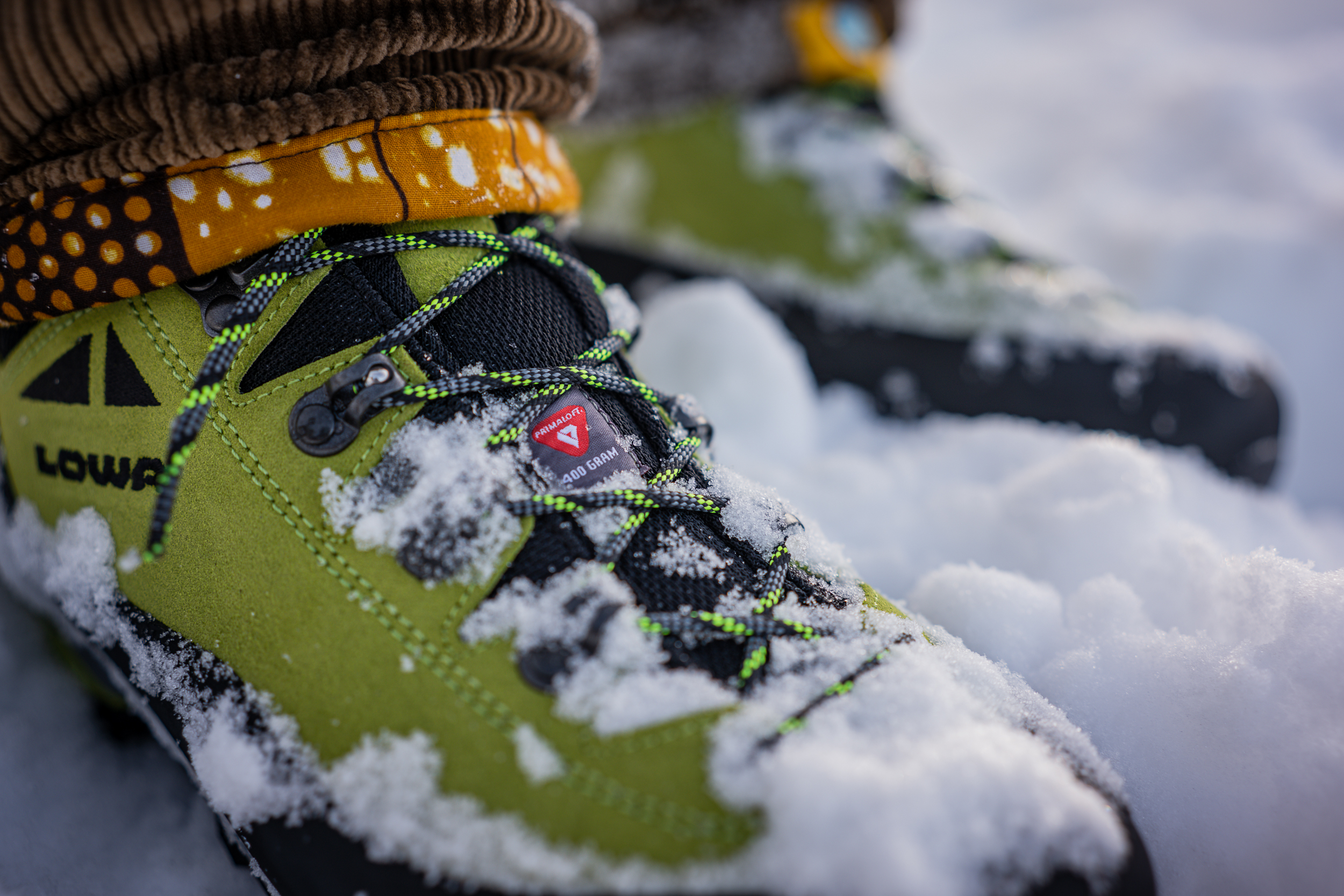 Green winter boots in snow with visible PrimaLoft 400g insulation label on tongue