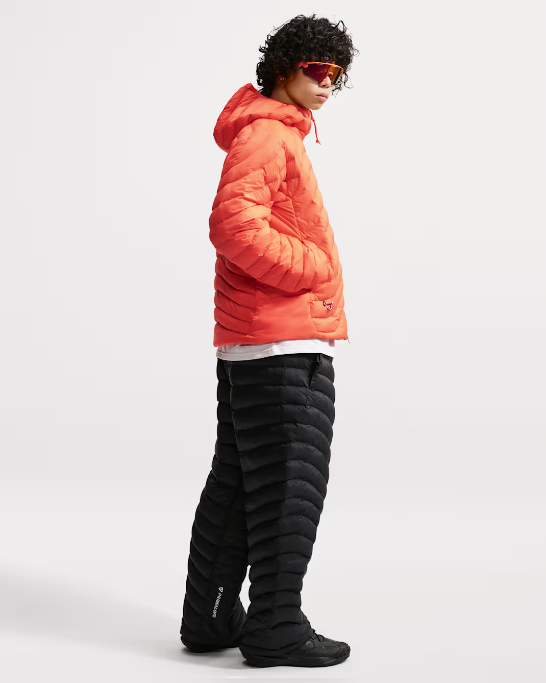 Man wearing an orange hooded jacket and black quilted pants, side view.
