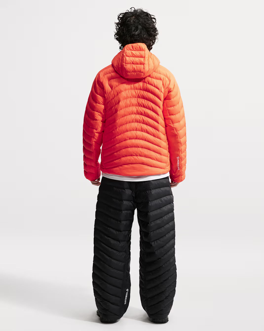 Man wearing an orange hooded jacket and black quilted pants, back view.